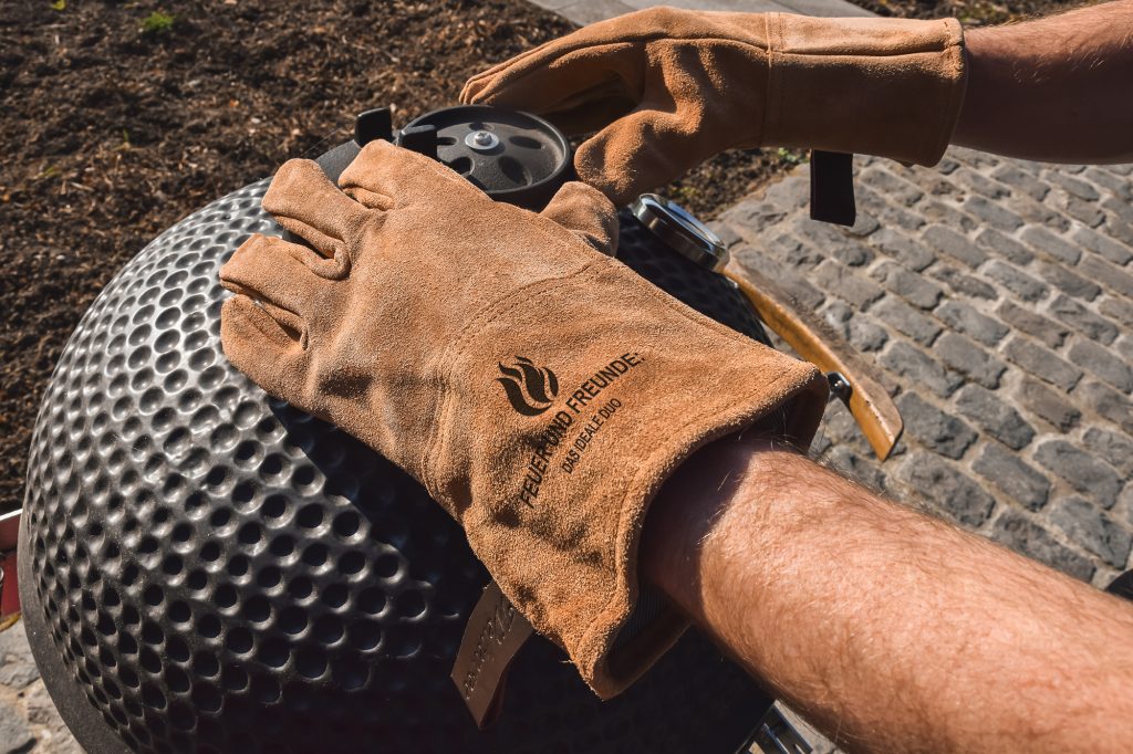 Hand in einem personalisierten Grillhandschuh aus Leder an einem Kugelgrill