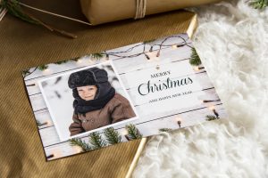 Weihnachtskarte mit Kinderfoto im Winter, Merry-Christmas-Schriftzug und Lichterkette
