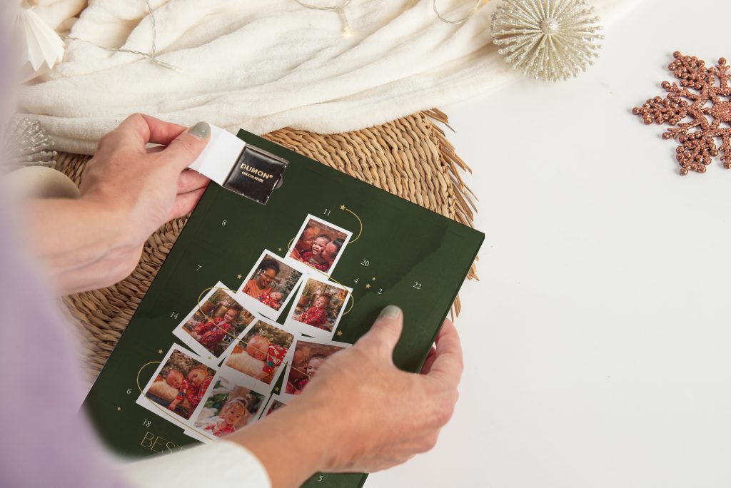 Hände öffnen ein Türchen an einem grünen Foto-Adventskalender mit Familienfotos in Tannenbaumform