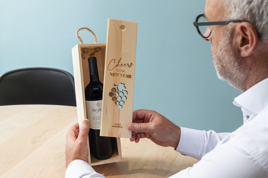 Mann öffnet eine personalisierte Weinkiste aus Holz mit einer Flasche Rotwein