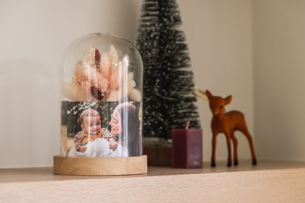 Glasglocke mit Trockenblumen und Familienfoto neben einem kleinen Tannenbaum und einer Rehfigur
