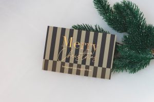 Weihnachtskarte mit Streifen-Motiv und Merry-Christmas-Schriftzug in Goldfolie neben Tannenzweig