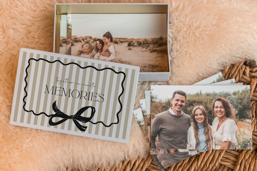 Fotobox mit gestreiftem Deckel und dem Schriftzug „Memories“ neben ausgedruckten Familienfotos
