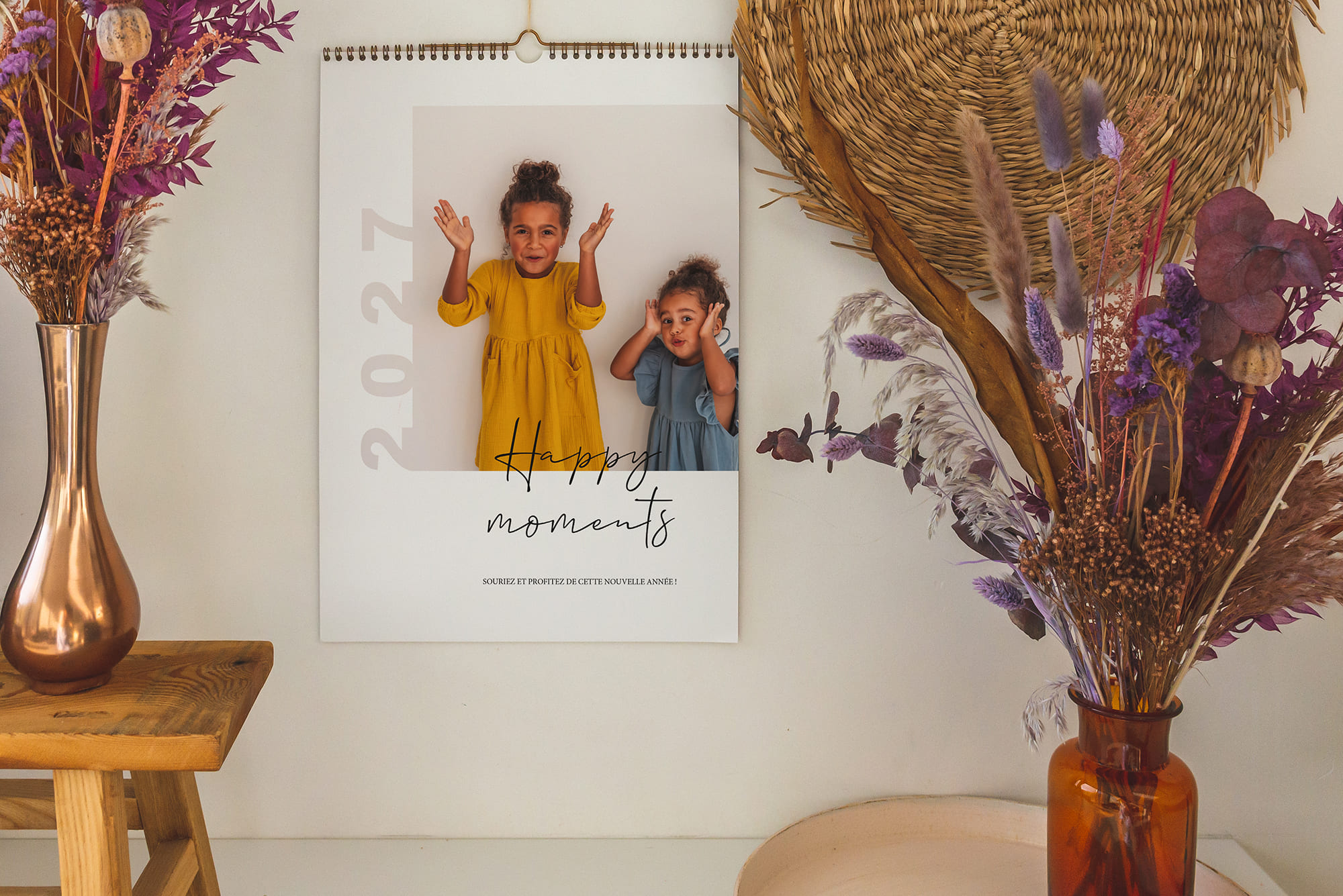 Wandkalender 2027 mit Kinderfoto und Schriftzug „Happy moments“ neben Trockenblumen